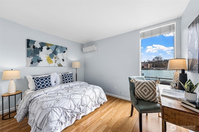 bedroom featuring baseboards, an AC wall unit, wood finished floors, and a water view