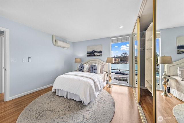 bedroom featuring an AC wall unit, baseboards, and wood finished floors