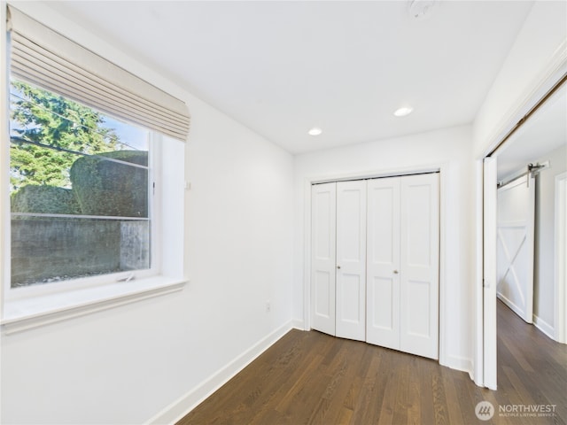 unfurnished bedroom featuring a barn door, recessed lighting, baseboards, a closet, and dark wood finished floors