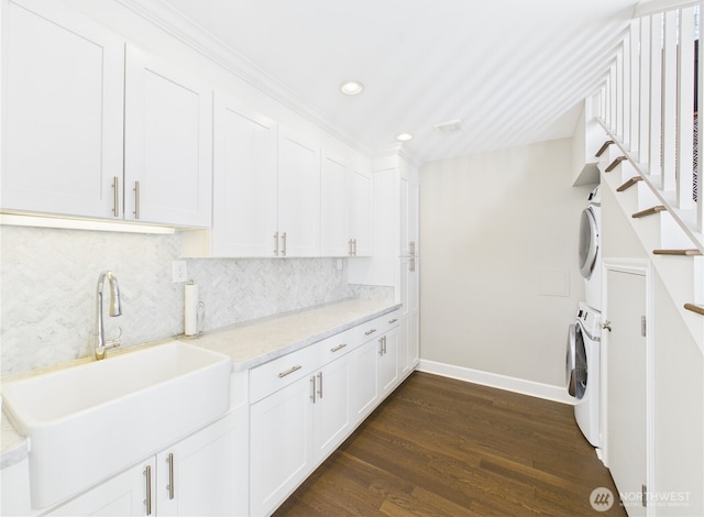 clothes washing area with stacked washer and dryer, a sink, baseboards, cabinet space, and dark wood-style floors