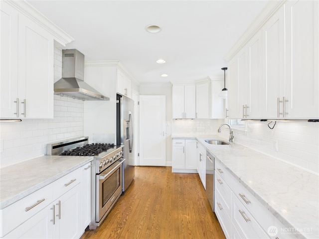 kitchen with stainless steel appliances, white cabinetry, a sink, and wall chimney range hood