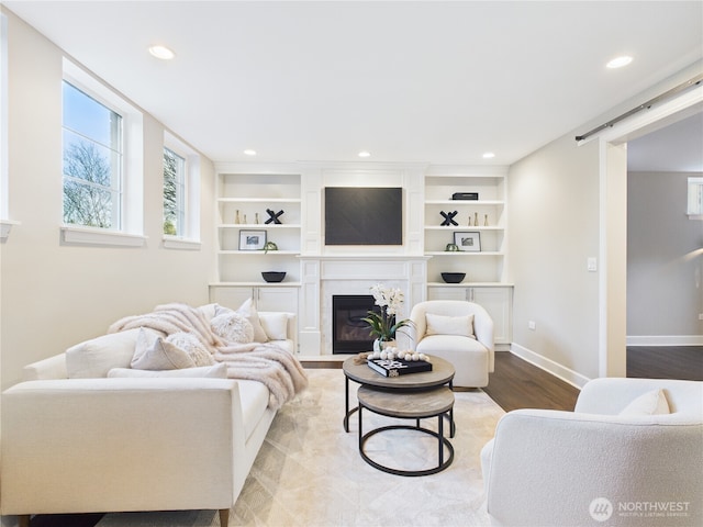 living area featuring recessed lighting, a barn door, a fireplace with flush hearth, wood finished floors, and baseboards