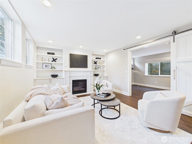 living room with recessed lighting, a barn door, a fireplace with flush hearth, wood finished floors, and baseboards