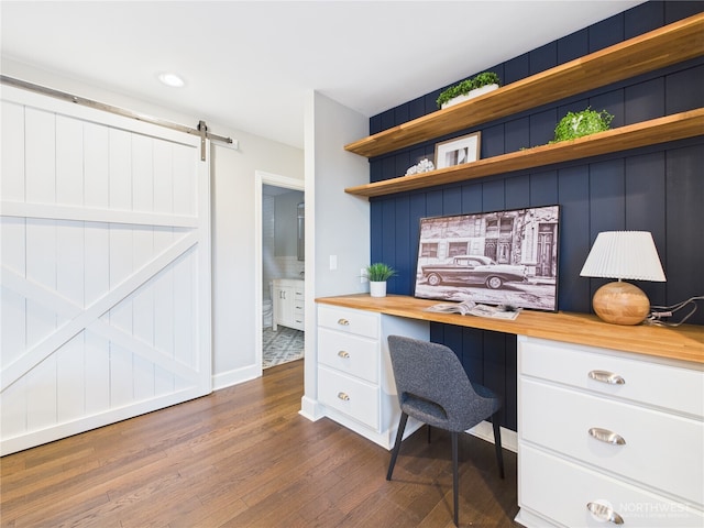 home office featuring a barn door, built in study area, dark wood finished floors, and baseboards