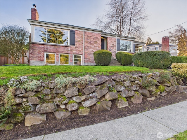 view of front of house featuring a chimney, fence, a front lawn, and brick siding