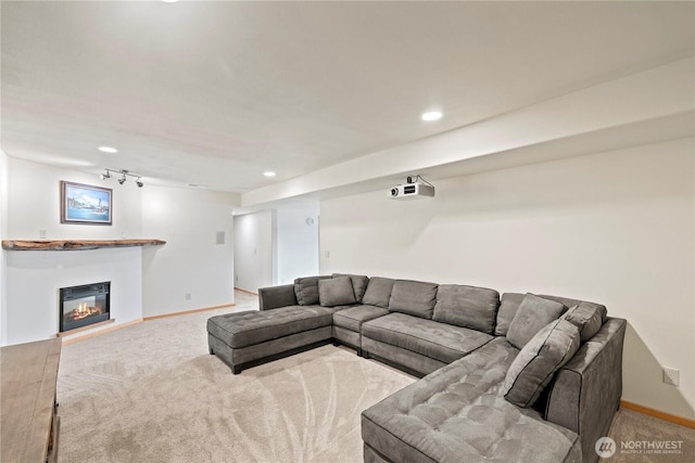 carpeted living area featuring a glass covered fireplace, rail lighting, baseboards, and recessed lighting