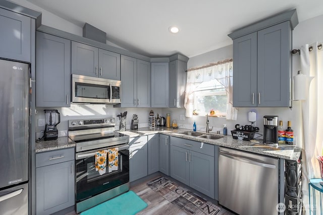 kitchen with light stone counters, appliances with stainless steel finishes, gray cabinets, and a sink