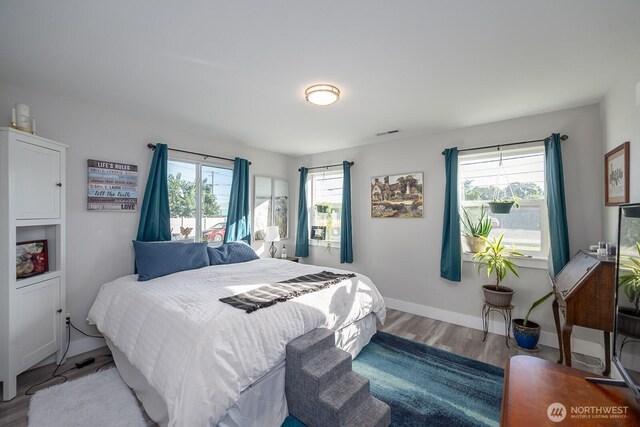 bedroom featuring multiple windows, wood finished floors, visible vents, and baseboards