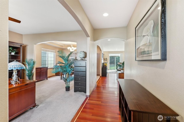 corridor with arched walkways, a healthy amount of sunlight, baseboards, and wood finished floors