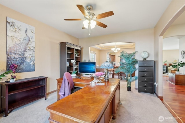 office area featuring baseboards, arched walkways, light colored carpet, and ceiling fan with notable chandelier