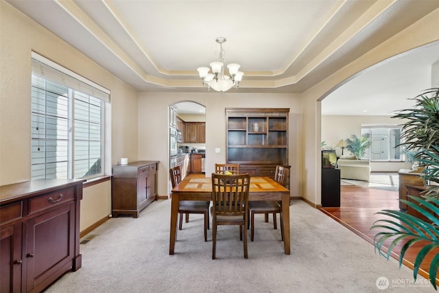 dining space featuring baseboards, light colored carpet, arched walkways, and a chandelier