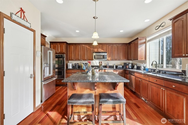 kitchen featuring a kitchen island, dark wood finished floors, a sink, stainless steel appliances, and a kitchen breakfast bar