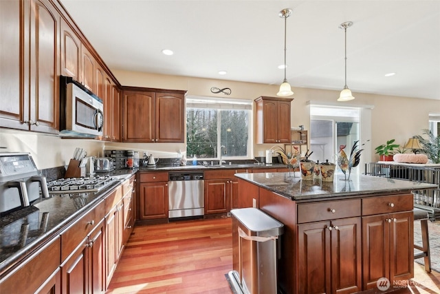 kitchen with light wood-style flooring, a sink, dark stone countertops, a center island, and stainless steel appliances