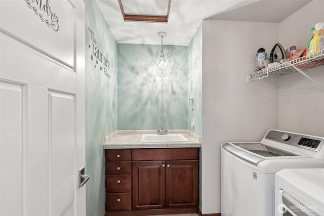 clothes washing area with laundry area, washer and dryer, an inviting chandelier, and a sink