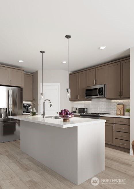 kitchen featuring pendant lighting, tasteful backsplash, appliances with stainless steel finishes, a kitchen island with sink, and a sink