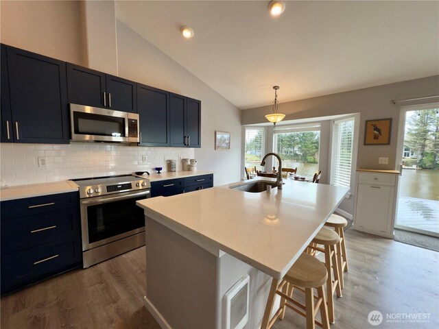 kitchen featuring appliances with stainless steel finishes, vaulted ceiling, light countertops, light wood-style floors, and a sink