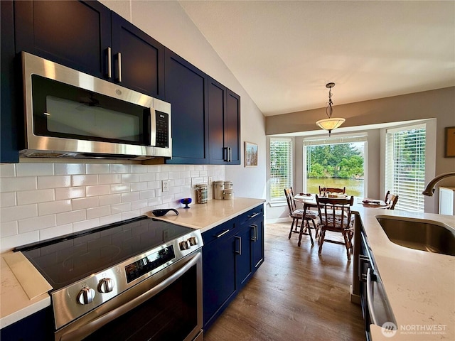 kitchen featuring appliances with stainless steel finishes, a sink, vaulted ceiling, blue cabinetry, and backsplash