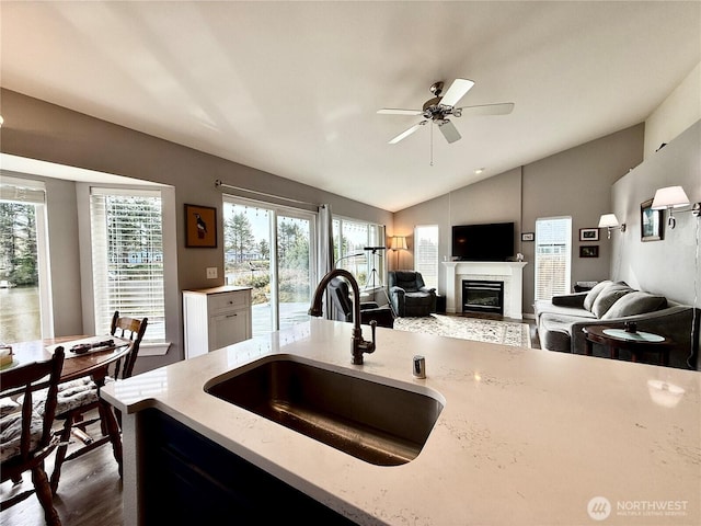 kitchen featuring light stone counters, lofted ceiling, a ceiling fan, a glass covered fireplace, and a sink