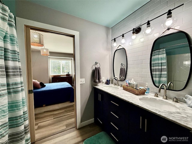 ensuite bathroom with double vanity, wood finished floors, a sink, and baseboards