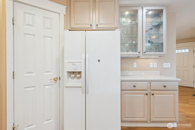 kitchen featuring light wood-style flooring, white refrigerator with ice dispenser, light countertops, light brown cabinetry, and glass insert cabinets