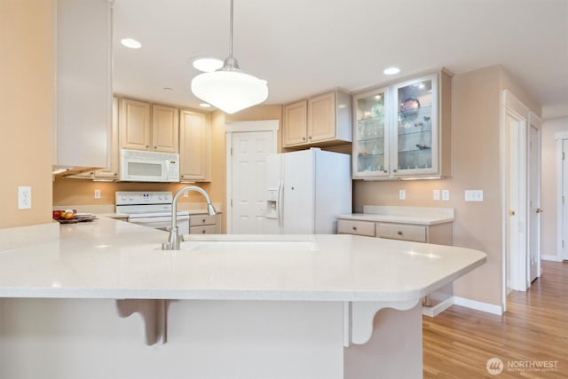 kitchen featuring light countertops, glass insert cabinets, a sink, white appliances, and a peninsula