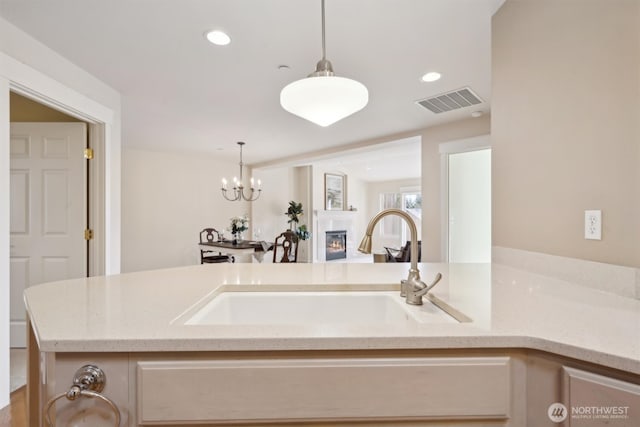 kitchen featuring a glass covered fireplace, a sink, visible vents, and light stone countertops