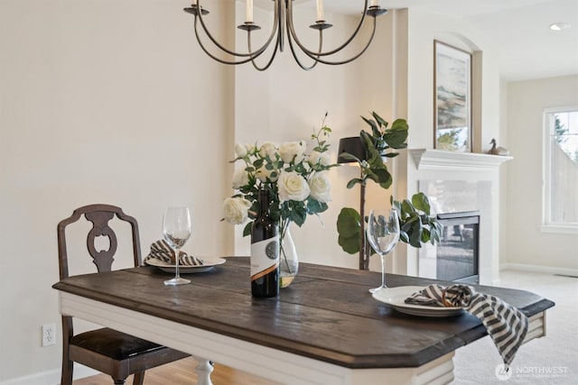 dining space featuring baseboards, carpet floors, a glass covered fireplace, and an inviting chandelier