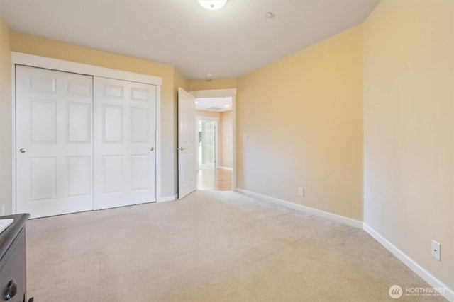 unfurnished bedroom featuring light carpet, a closet, and baseboards