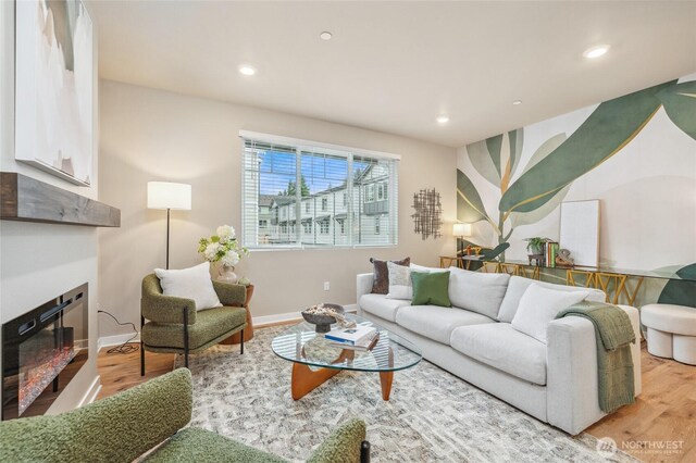 living room featuring light wood finished floors, recessed lighting, baseboards, and a glass covered fireplace