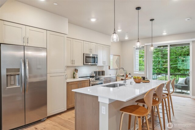 kitchen featuring stainless steel appliances, a sink, light countertops, light wood finished floors, and tasteful backsplash