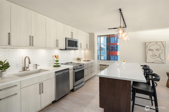 kitchen with stainless steel appliances, backsplash, a sink, light wood-type flooring, and a kitchen breakfast bar