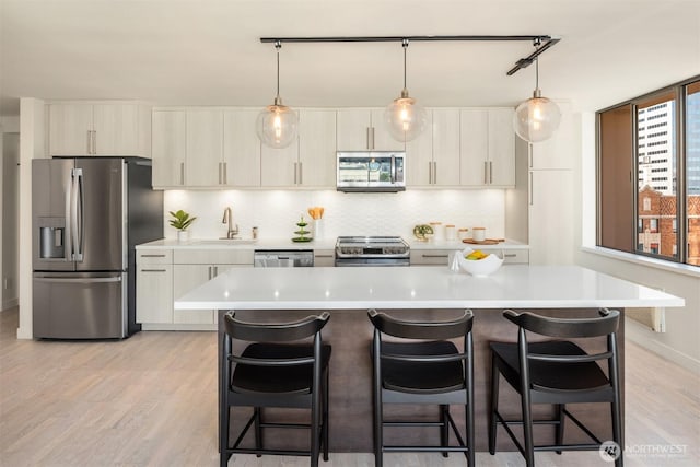 kitchen with appliances with stainless steel finishes, light countertops, a sink, and a kitchen breakfast bar