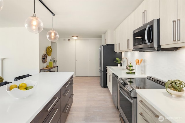 kitchen with stainless steel appliances, a sink, hanging light fixtures, light countertops, and tasteful backsplash