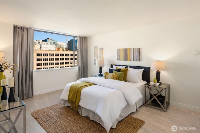 bedroom with a view of city, wood finished floors, and baseboards