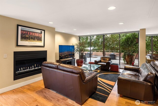 living area featuring a wall of windows, a warm lit fireplace, baseboards, and light wood finished floors