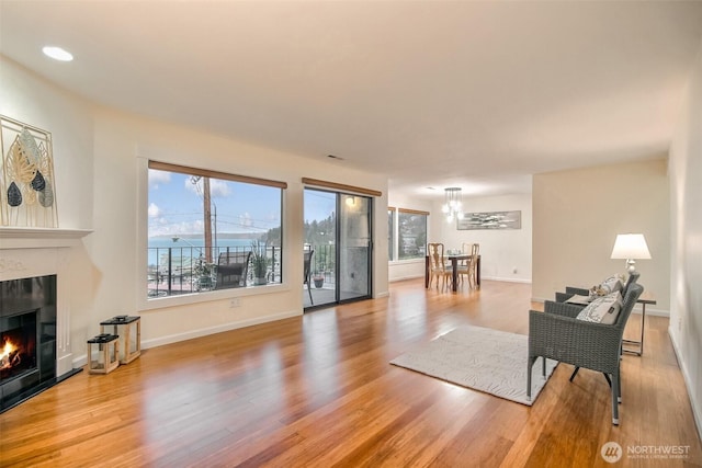 living area with a lit fireplace, baseboards, and wood finished floors