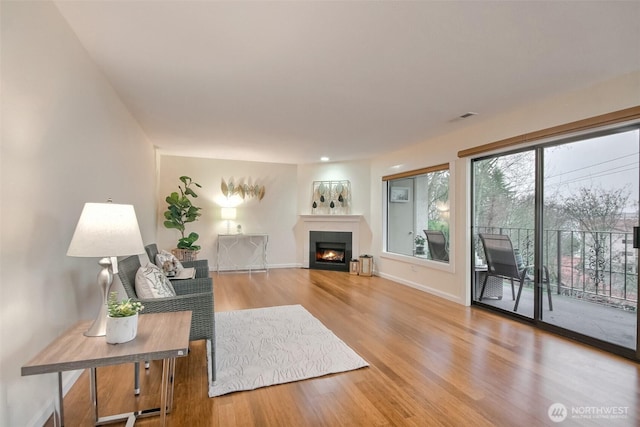 living area with a warm lit fireplace, baseboards, visible vents, and wood finished floors