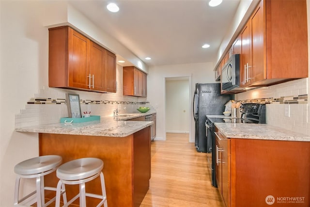 kitchen with brown cabinetry, light wood-style flooring, a breakfast bar area, a peninsula, and black appliances