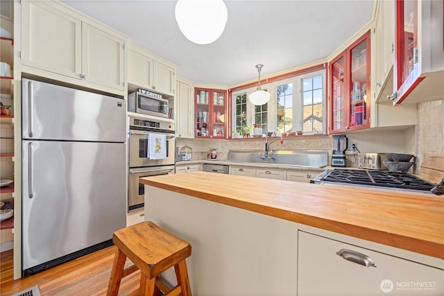 kitchen featuring stainless steel appliances, a peninsula, light wood-style floors, wooden counters, and glass insert cabinets