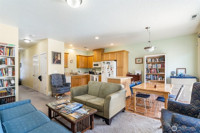 living area with a textured ceiling, light colored carpet, visible vents, and recessed lighting