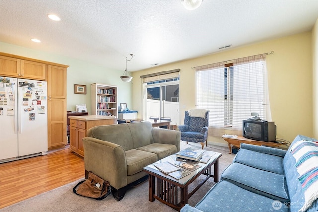 living area featuring light wood-type flooring, visible vents, a textured ceiling, and recessed lighting