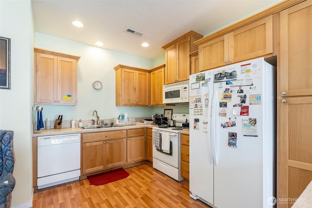 kitchen with white appliances, visible vents, light countertops, light wood-style floors, and a sink