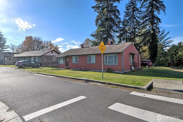 view of front of home with entry steps, roof with shingles, a chimney, and a front yard