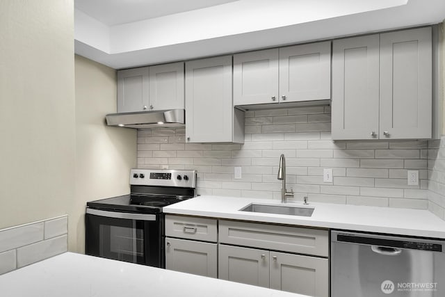 kitchen with gray cabinetry, under cabinet range hood, stainless steel appliances, a sink, and tasteful backsplash