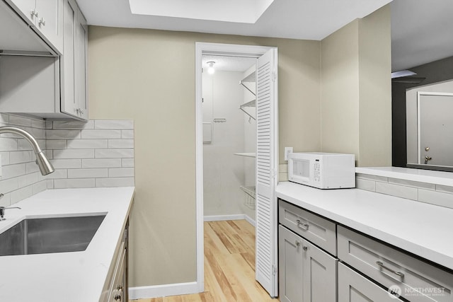 kitchen with decorative backsplash, white microwave, light wood-style flooring, gray cabinets, and a sink