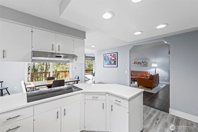 kitchen with white cabinets, light wood-style floors, black electric stovetop, light countertops, and under cabinet range hood