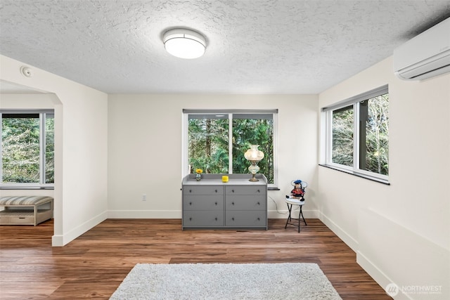 unfurnished room featuring a wall mounted air conditioner, a textured ceiling, baseboards, and wood finished floors