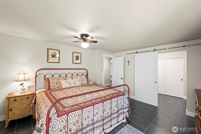 bedroom with dark tile patterned floors, a barn door, baseboards, and ceiling fan