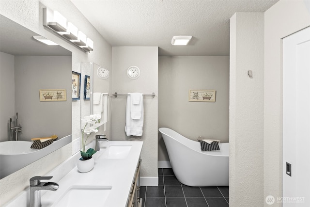 bathroom with a textured ceiling, a freestanding tub, tile patterned flooring, and a sink