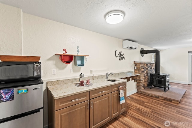 kitchen with black microwave, refrigerator, a sink, a wall mounted AC, and a wood stove